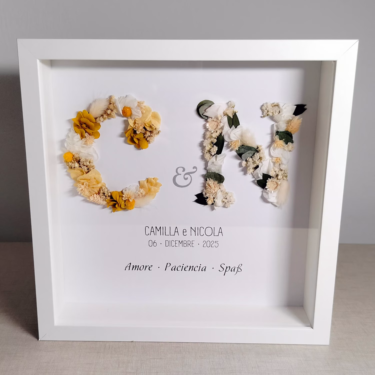 Cuadro con dos iniciales de flores preservadas y frase